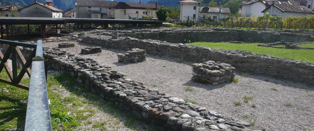 Ancient stone ruins with a wooden fence and houses in the background.