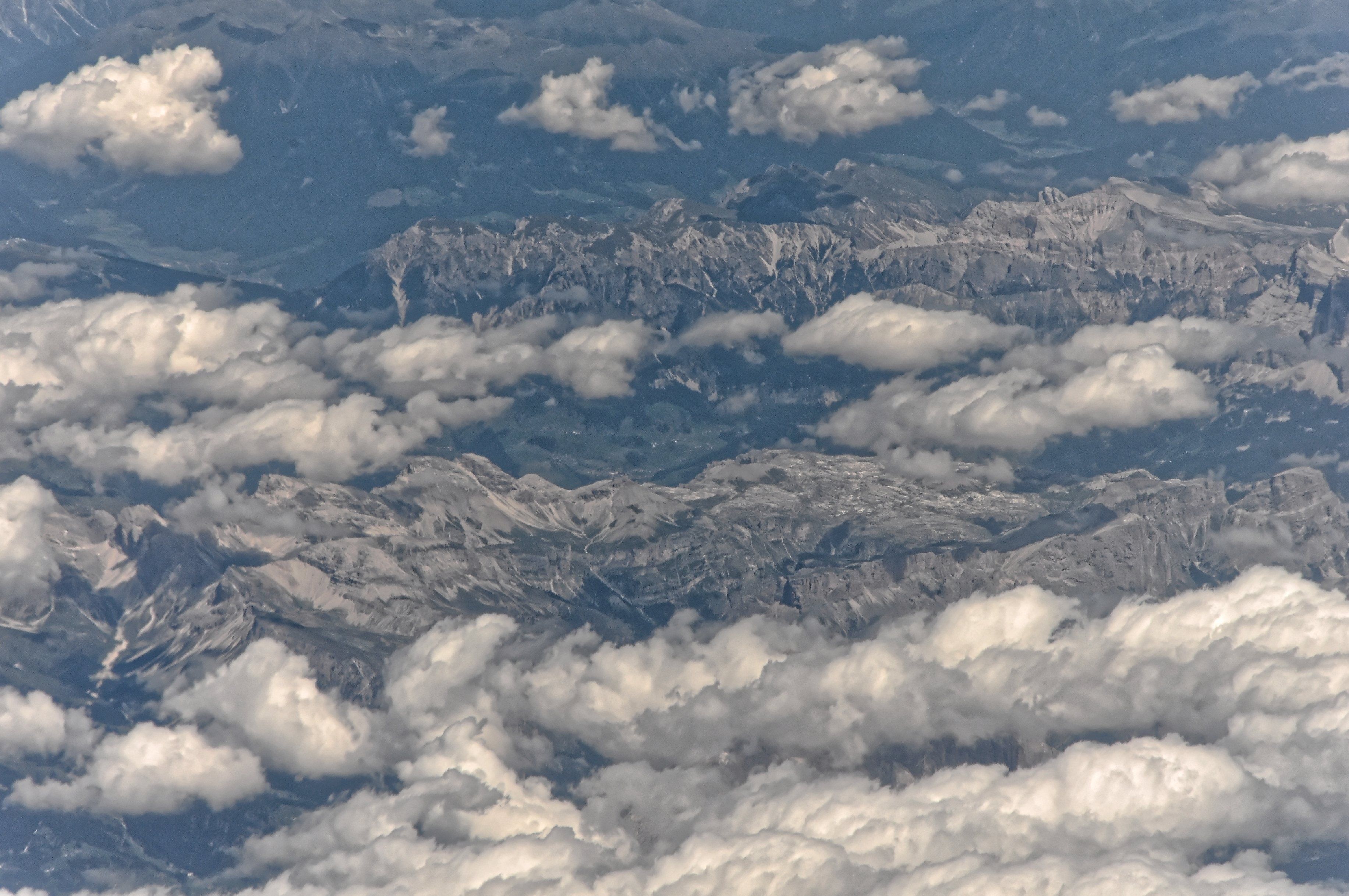 A mountainous landscape with snow-covered peaks and scattered clouds.