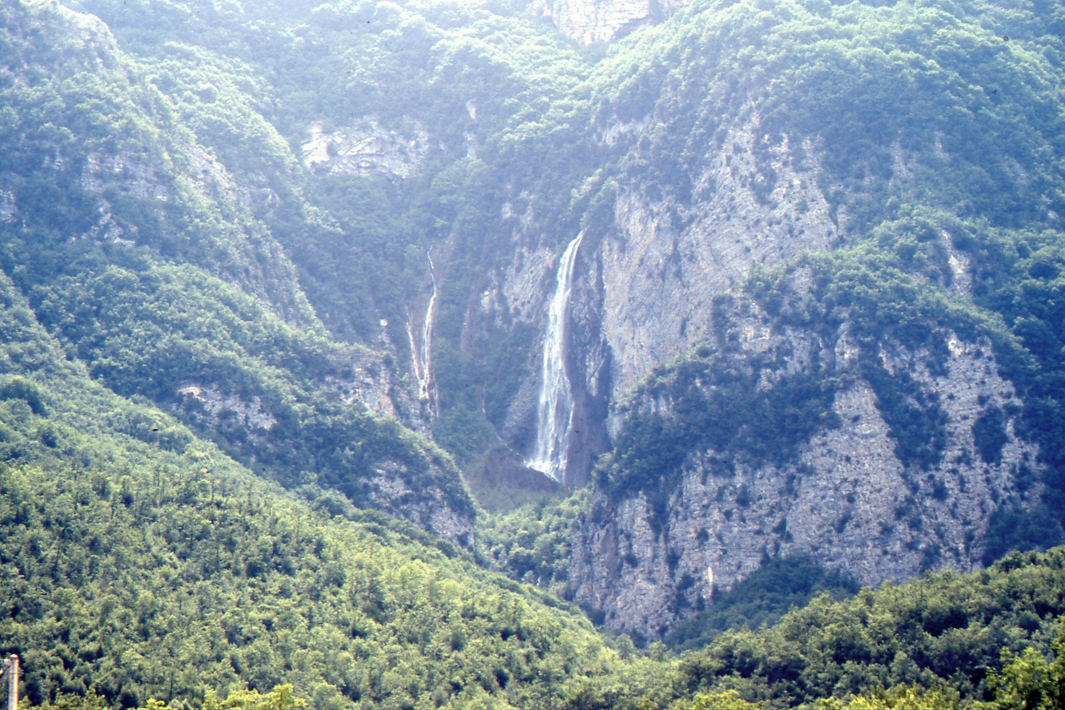A lush green valley with a waterfall cascading down a steep cliff.
