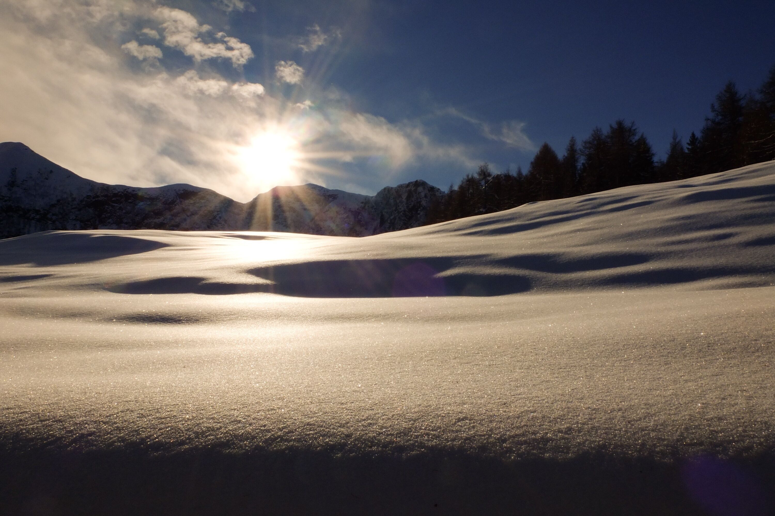 A snowy mountain landscape with the sun shining through the clouds.