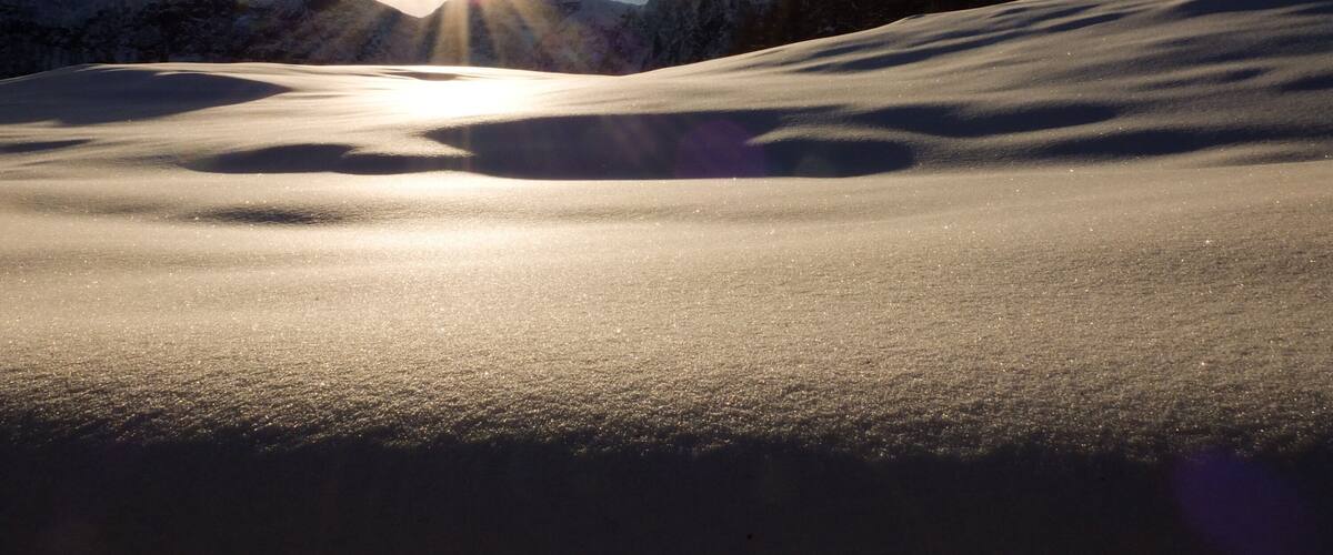 A snowy mountain landscape with the sun shining through the clouds.
