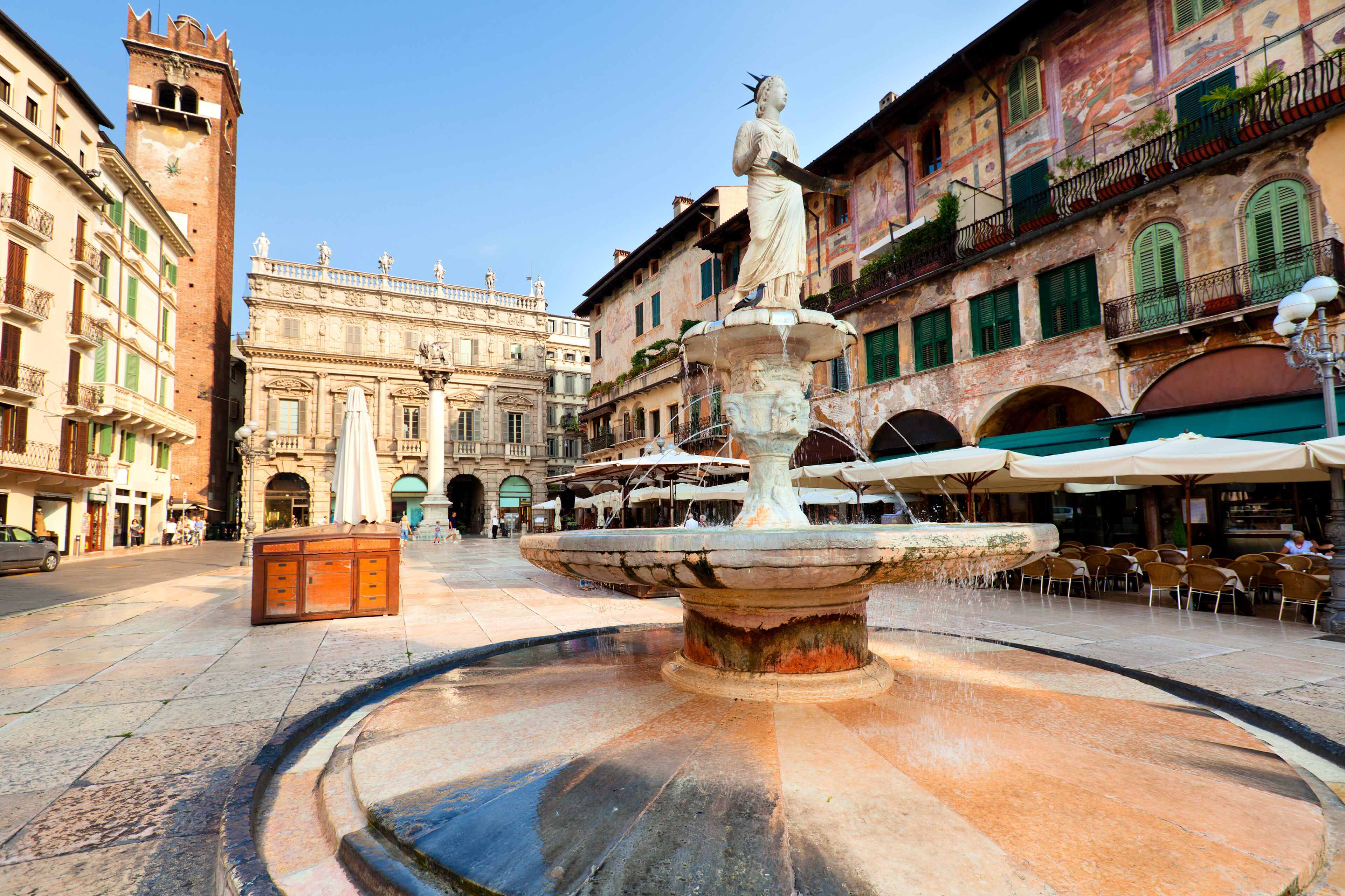 A historic fountain with a statue in the center, surrounded by classic European architecture and outdoor seating areas.