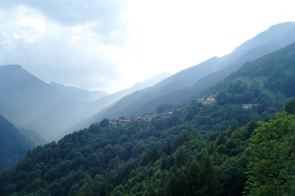 A mountainous landscape with dense forests and several buildings nestled among the hills.