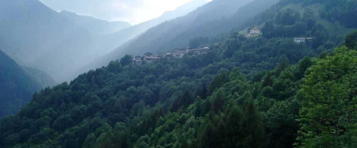 A mountainous landscape with dense forests and several buildings nestled among the hills.
