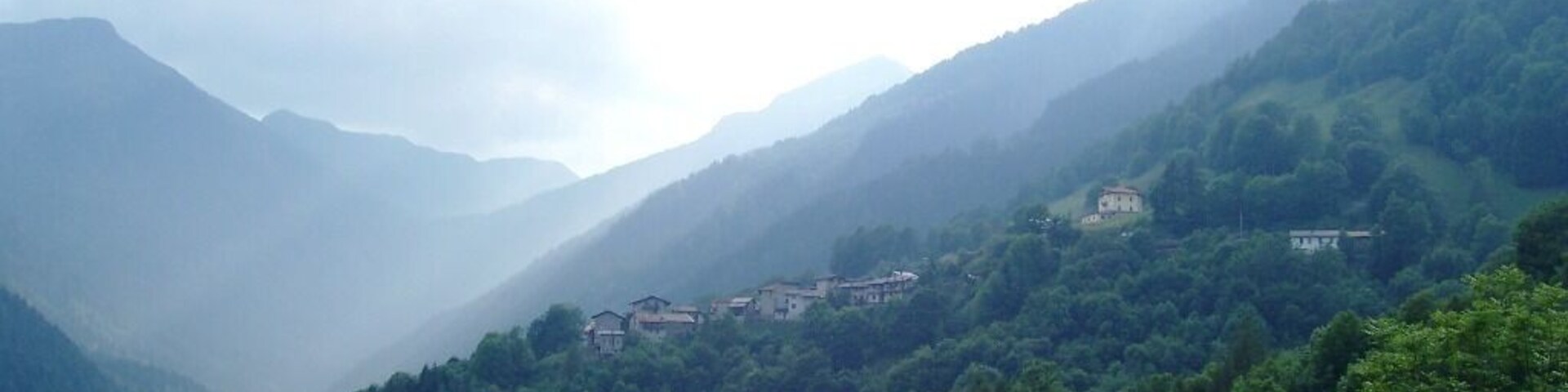 A mountainous landscape with dense forests and several buildings nestled among the hills.