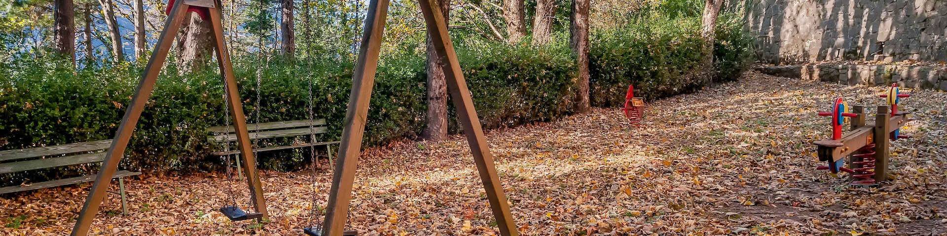Um parque com baloiço, gangorra e um muro de pedra.