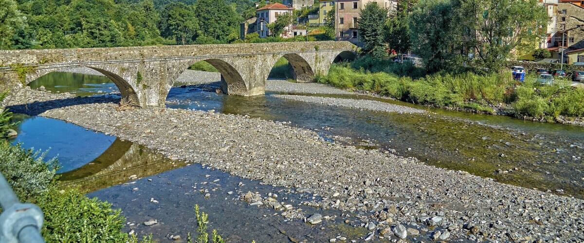 A stone bridge over a river, surrounded by houses and lush green hills.