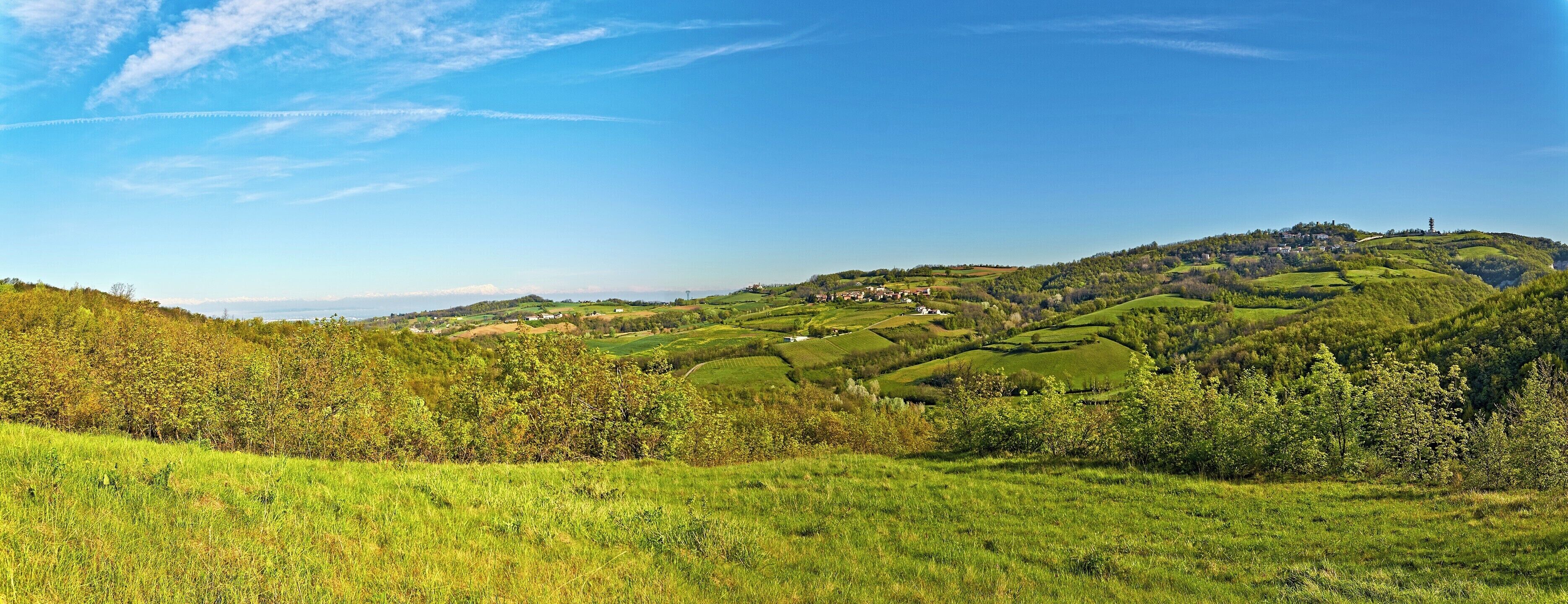 Rolling green hills, a clear blue sky, and scattered buildings on a hillside.