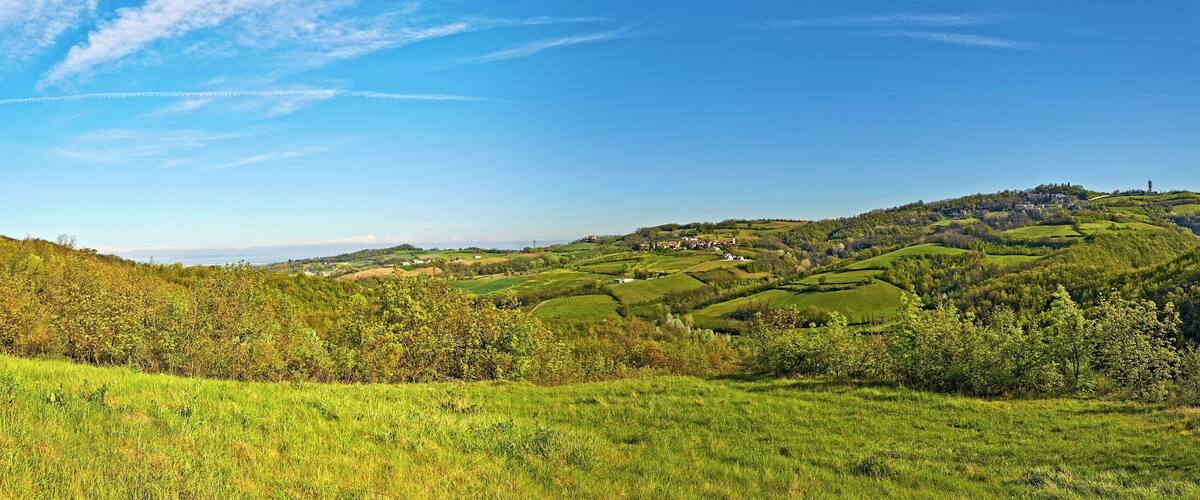 Rolling green hills, a clear blue sky, and scattered buildings on a hillside.