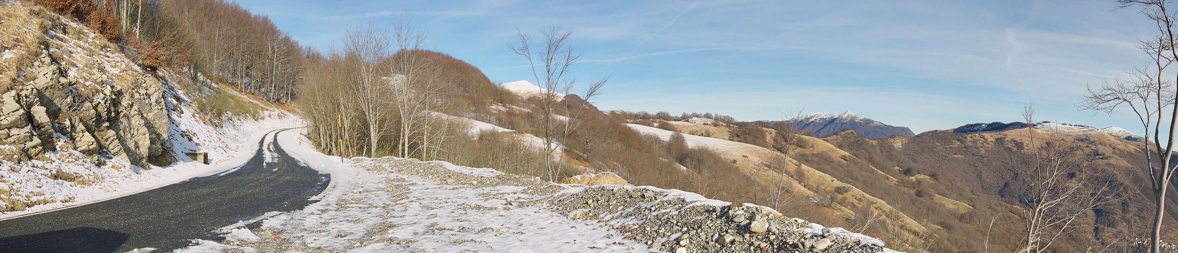 A winding road through a mountainous landscape with snow-covered slopes and rocky terrain.