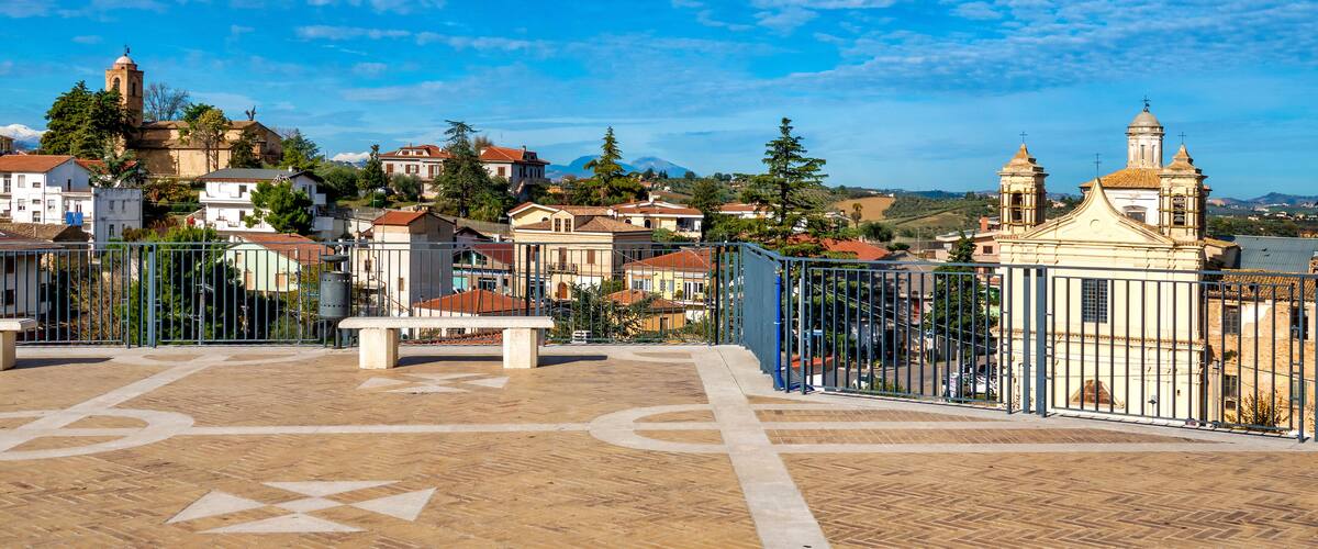 A town square with a tiled floor, a fountain, and a church with a bell tower.
