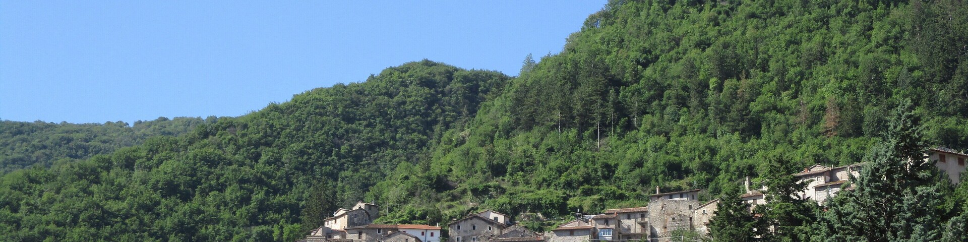 Un pueblo en una ladera con edificios tradicionales rodeados de frondosos árboles verdes.