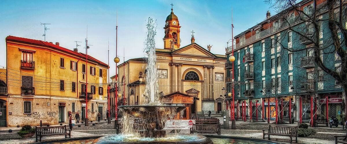 A historic fountain in a square surrounded by colorful buildings.