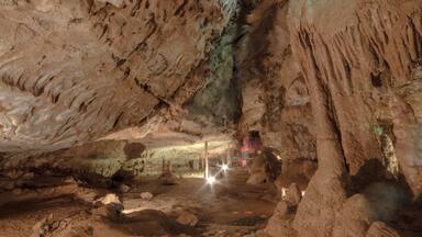 A cave with stalactites and stalagmites, a water pool, and a light source.