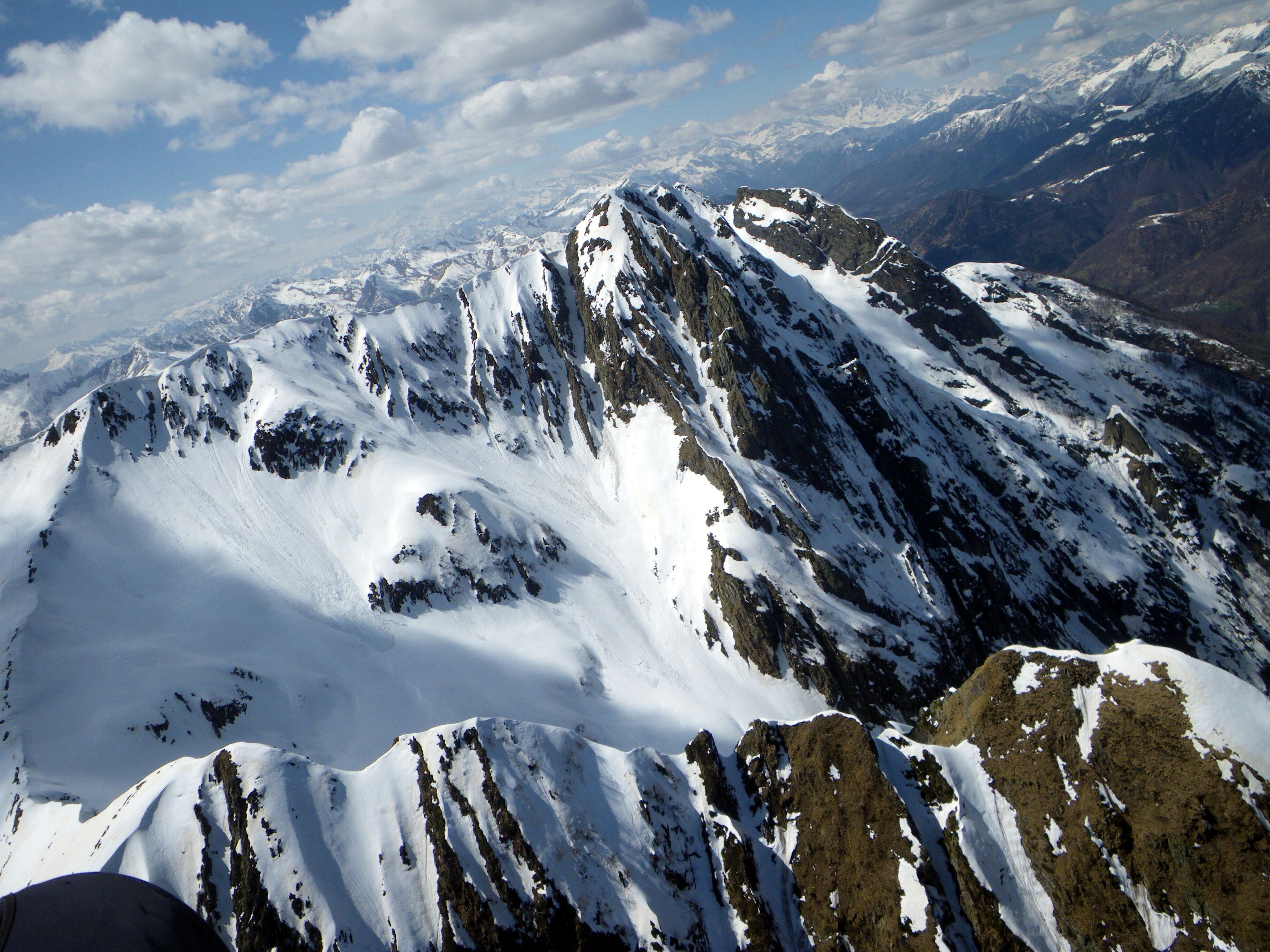 A snow-covered mountain peak with rugged terrain and distant snow-capped mountains.