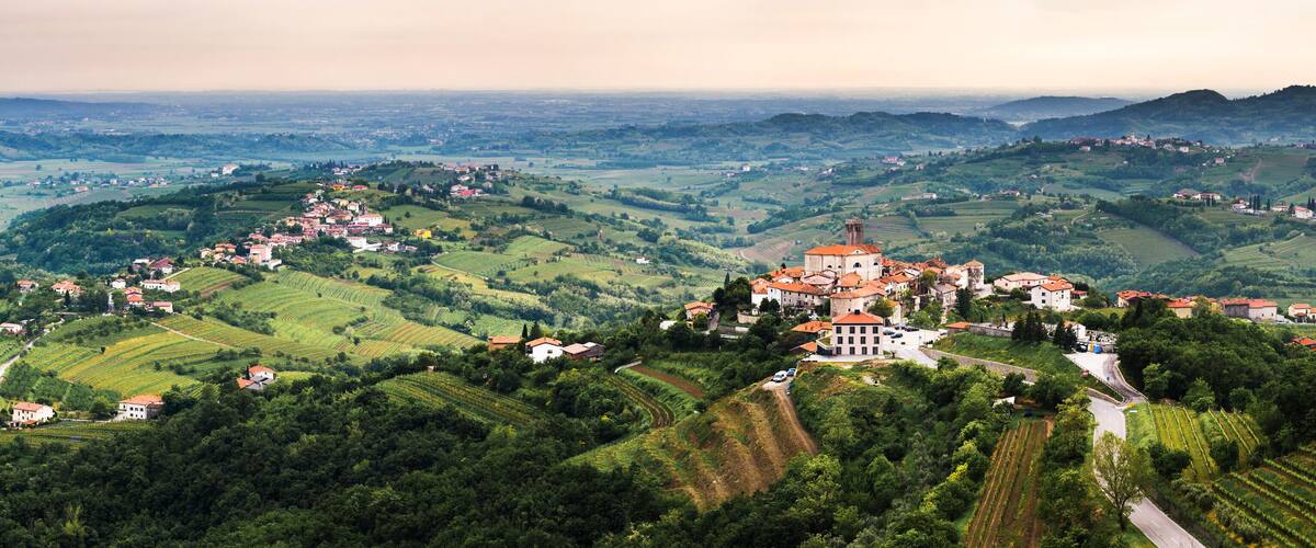 A mountainous landscape with terraced vineyards, a prominent church with a red roof, and scattered houses.
