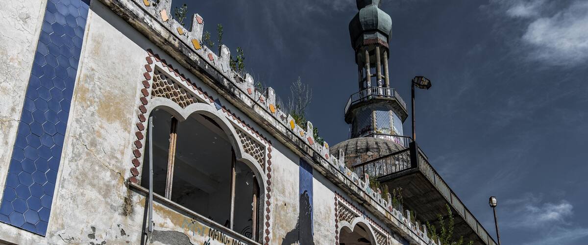 A historic building with intricate tile work, a prominent minaret, and graffiti.