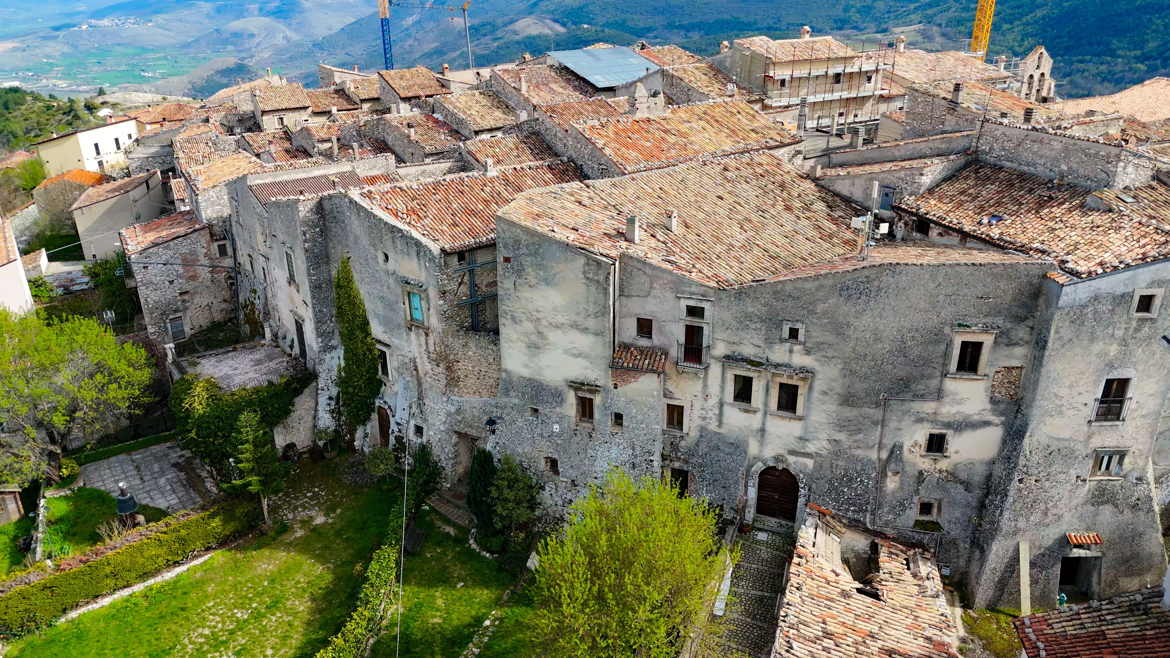 A historic town with terracotta-tiled roofs, stone buildings, and a mountainous backdrop.