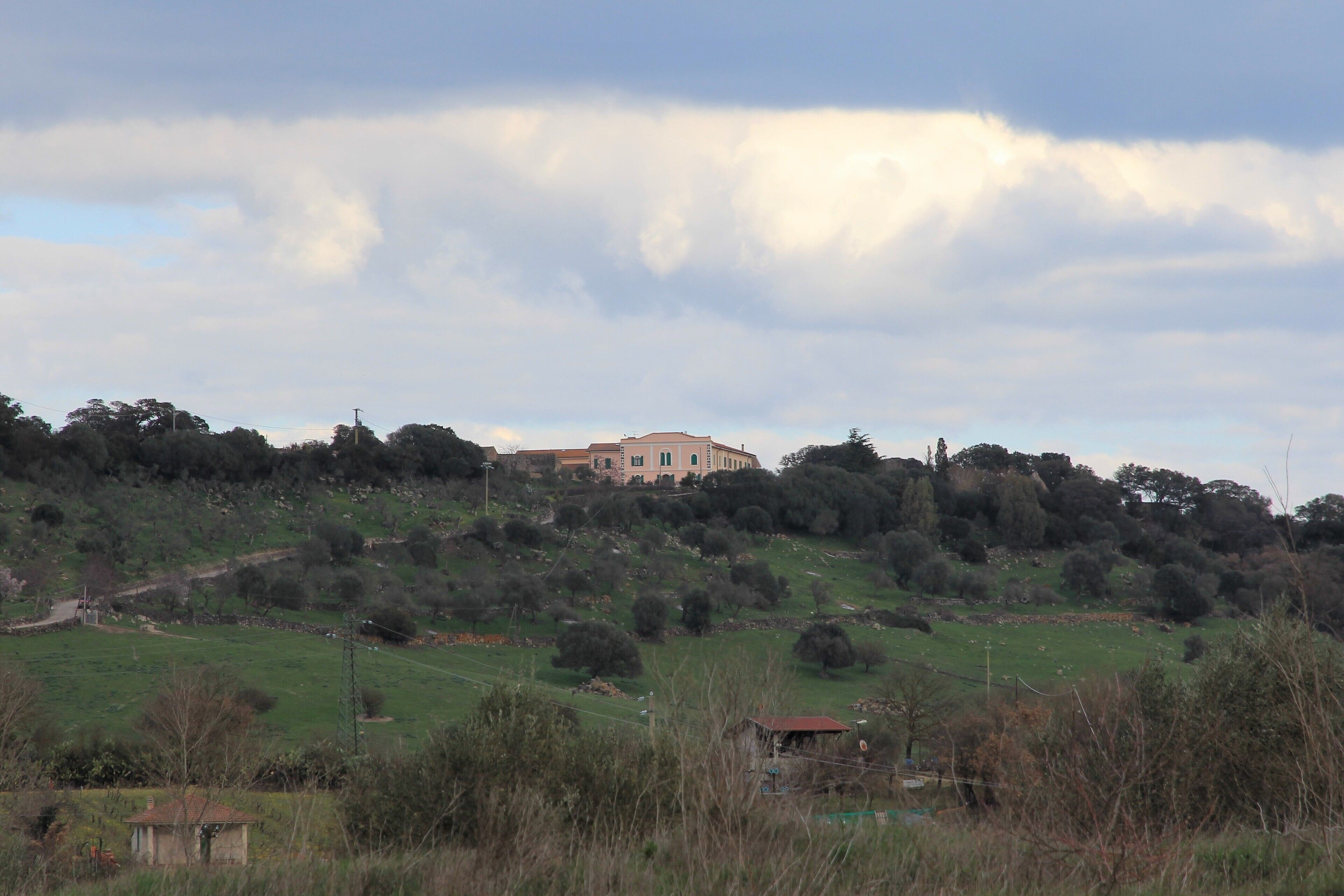 A large building on a hill with a cloudy sky.