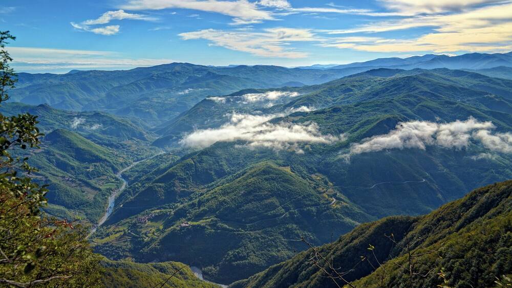 A mountainous landscape with lush green valleys and a river winding through the terrain.