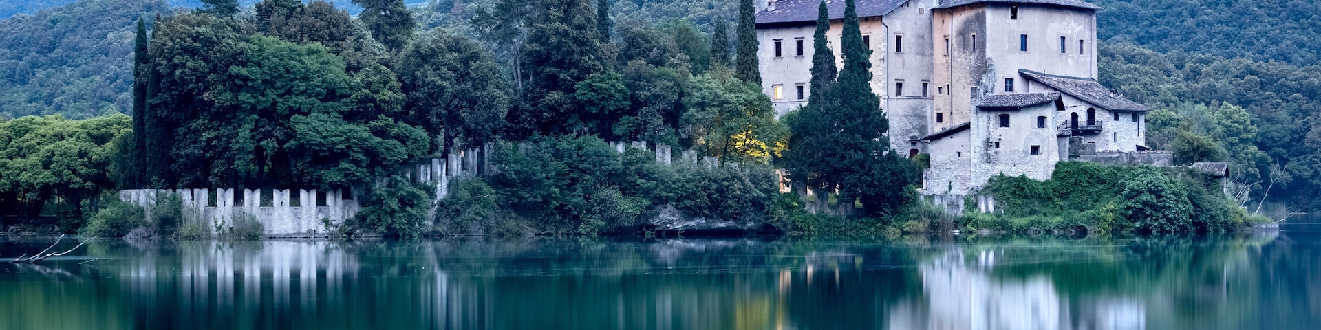Un castillo histórico a orillas de un lago, rodeado de exuberante vegetación y montañas.