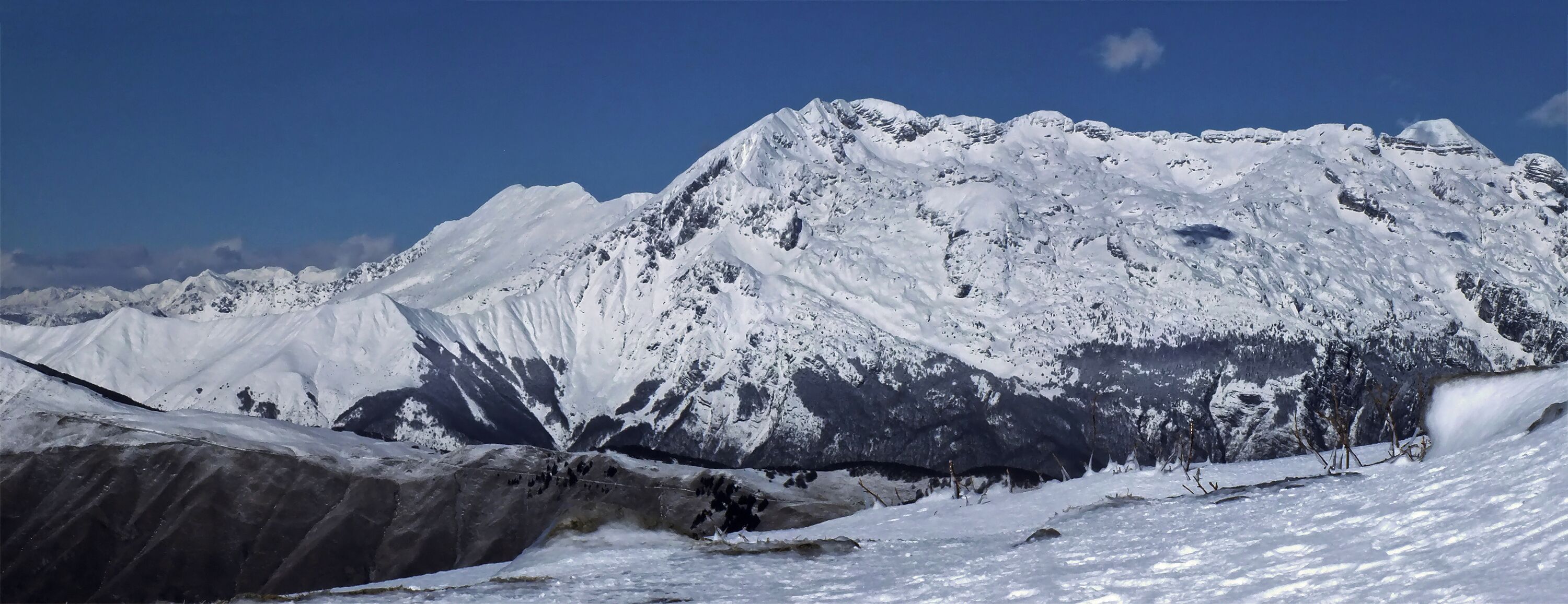 A snow-covered mountain range with rugged peaks and a clear blue sky.