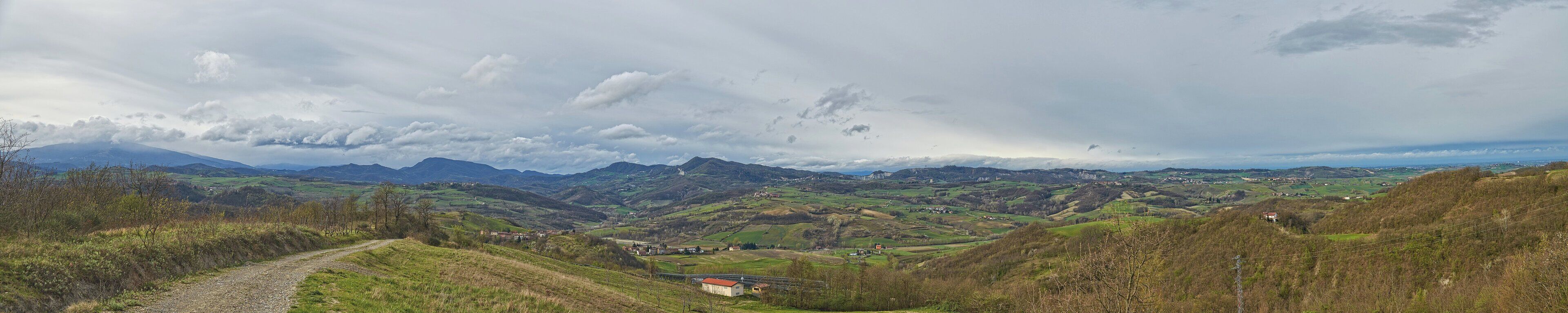 A valley with a dirt path, rolling hills, and distant mountains under a cloudy sky.