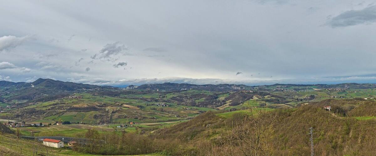 A valley with a dirt path, rolling hills, and distant mountains under a cloudy sky.