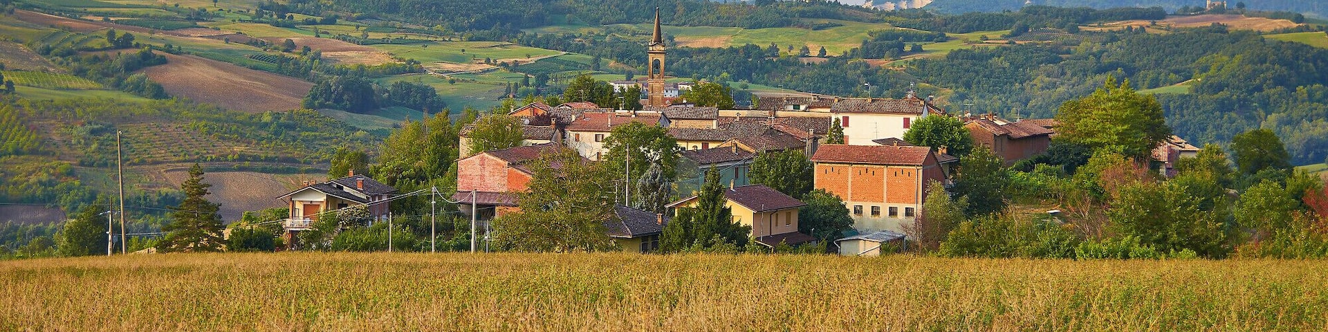 A rural village with a church tower, surrounded by rolling hills and fields.