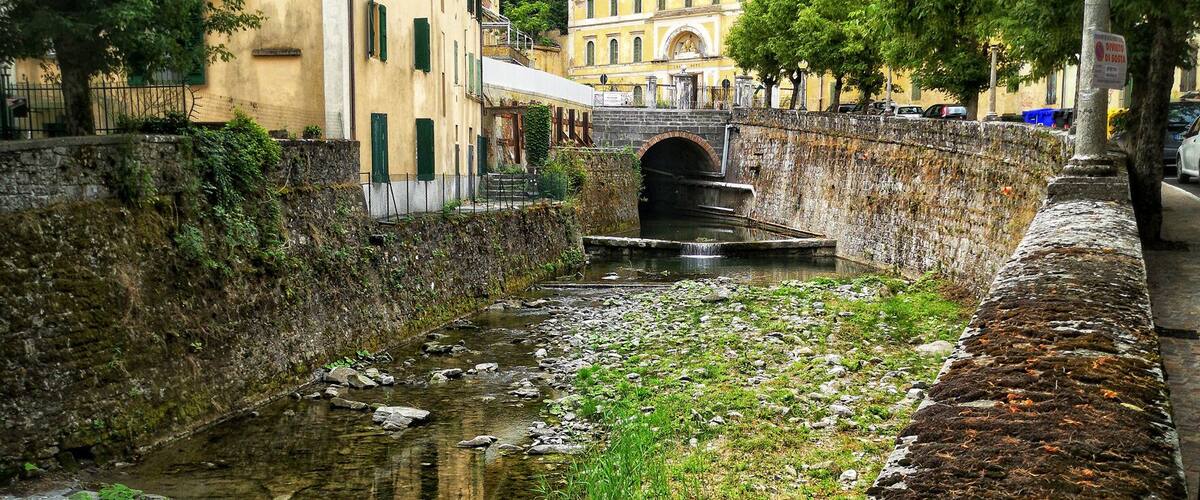 A stone bridge over a canal with buildings and trees in the background.