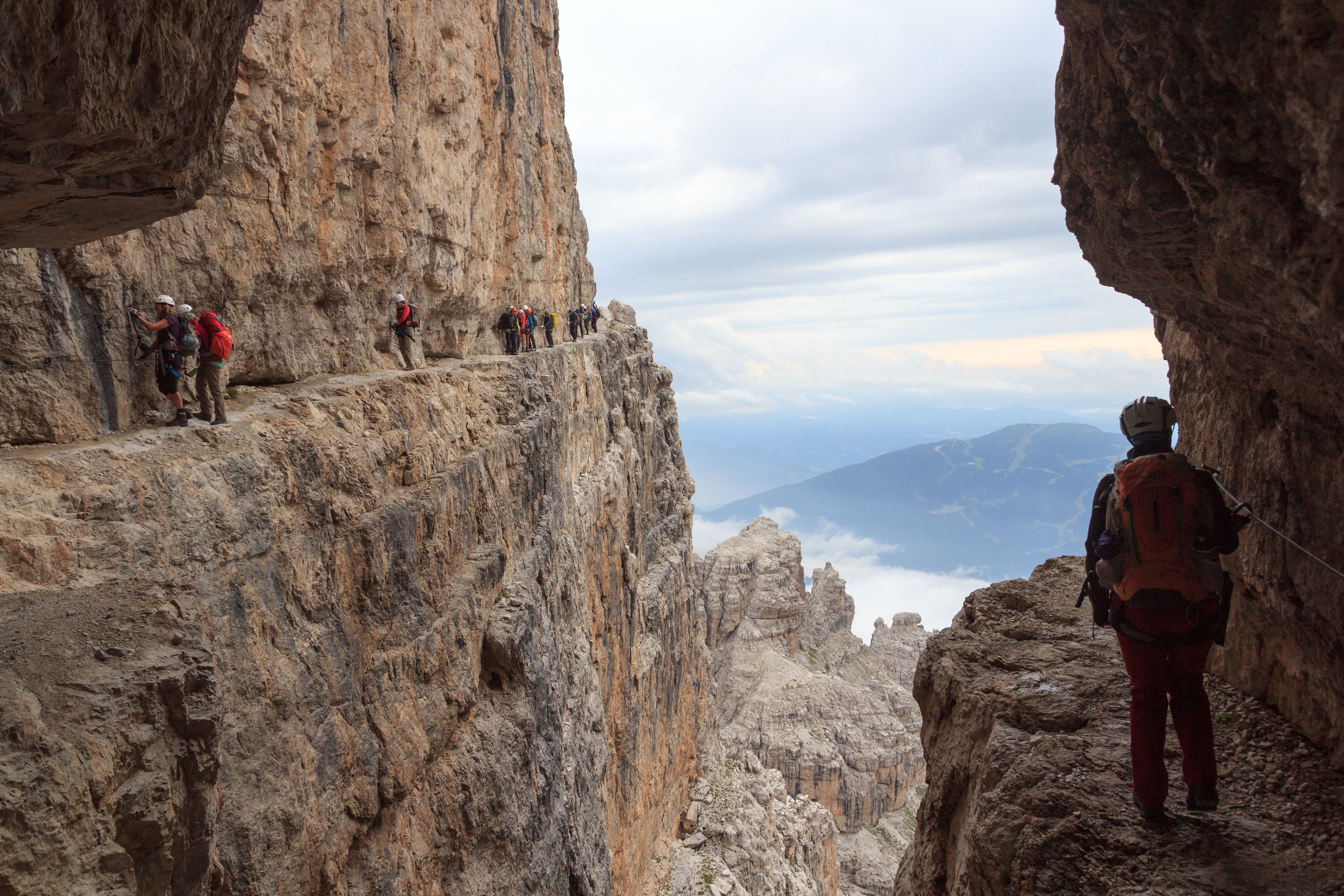 Un grupo de excursionistas en una empinada cresta montañosa con vistas a montañas y nubes distantes.