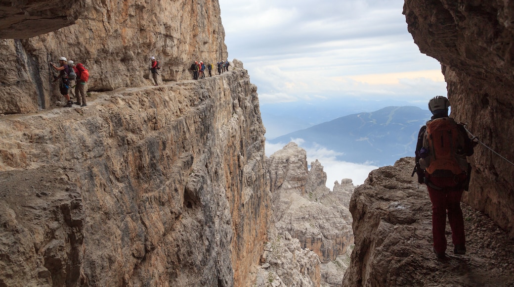 Un grupo de excursionistas en una empinada cresta montañosa con vistas a montañas y nubes distantes.