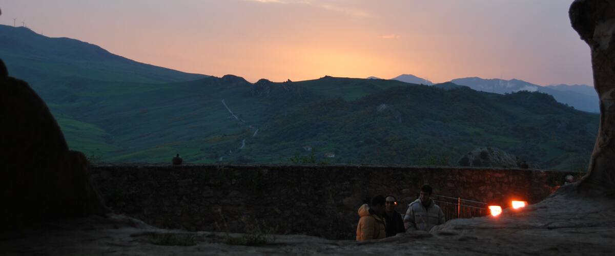 A sunset over a mountainous landscape viewed from a cave entrance.