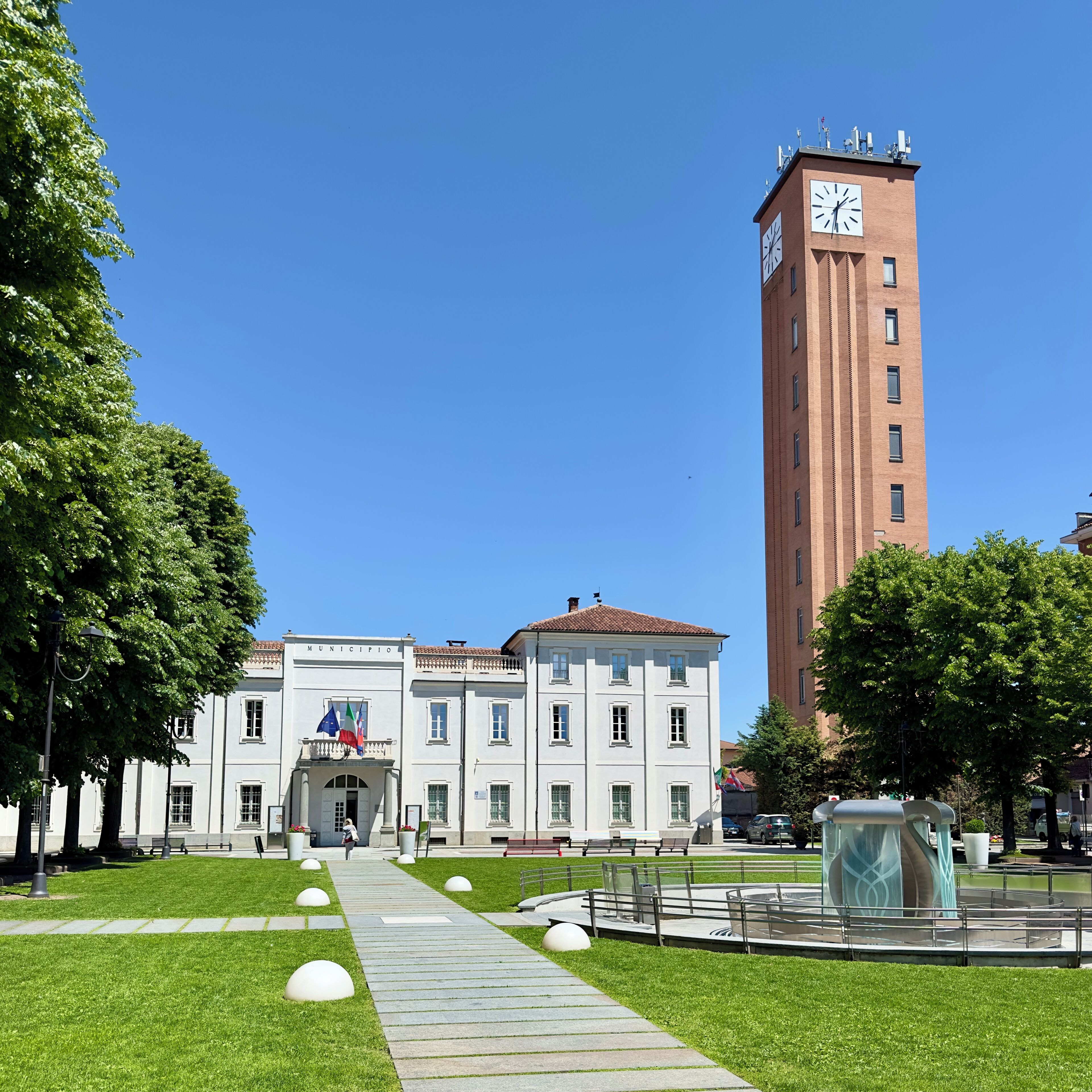 A building with a clock tower, a paved walkway, and green trees.