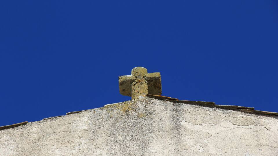 A weathered stone cross atop a building with a clear blue sky in the background.