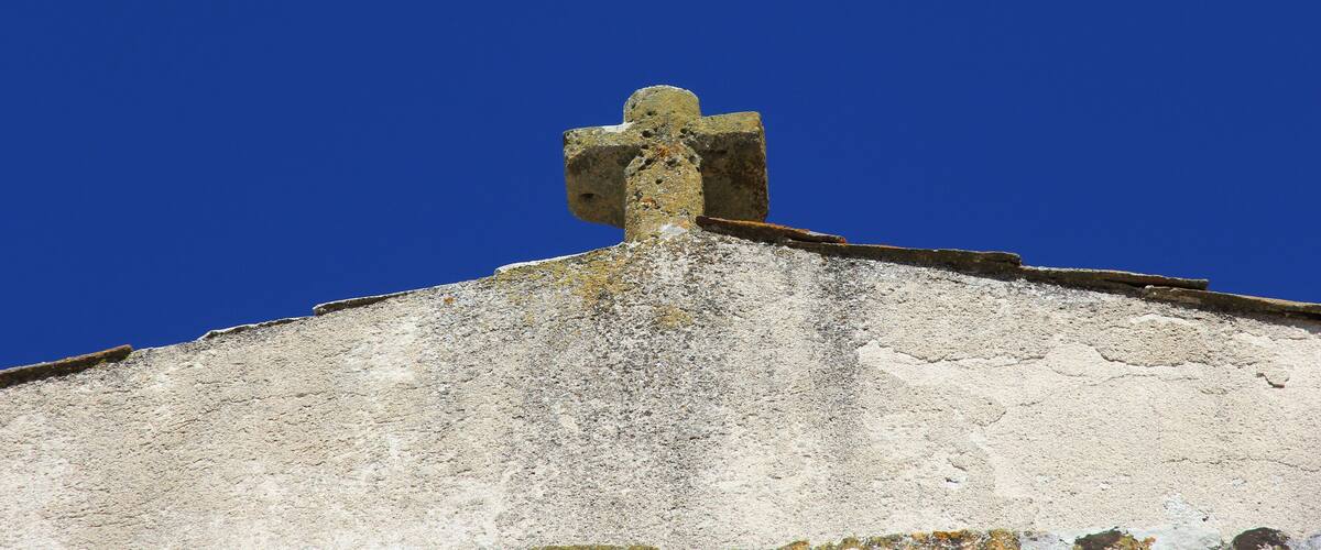 A weathered stone cross atop a building with a clear blue sky in the background.