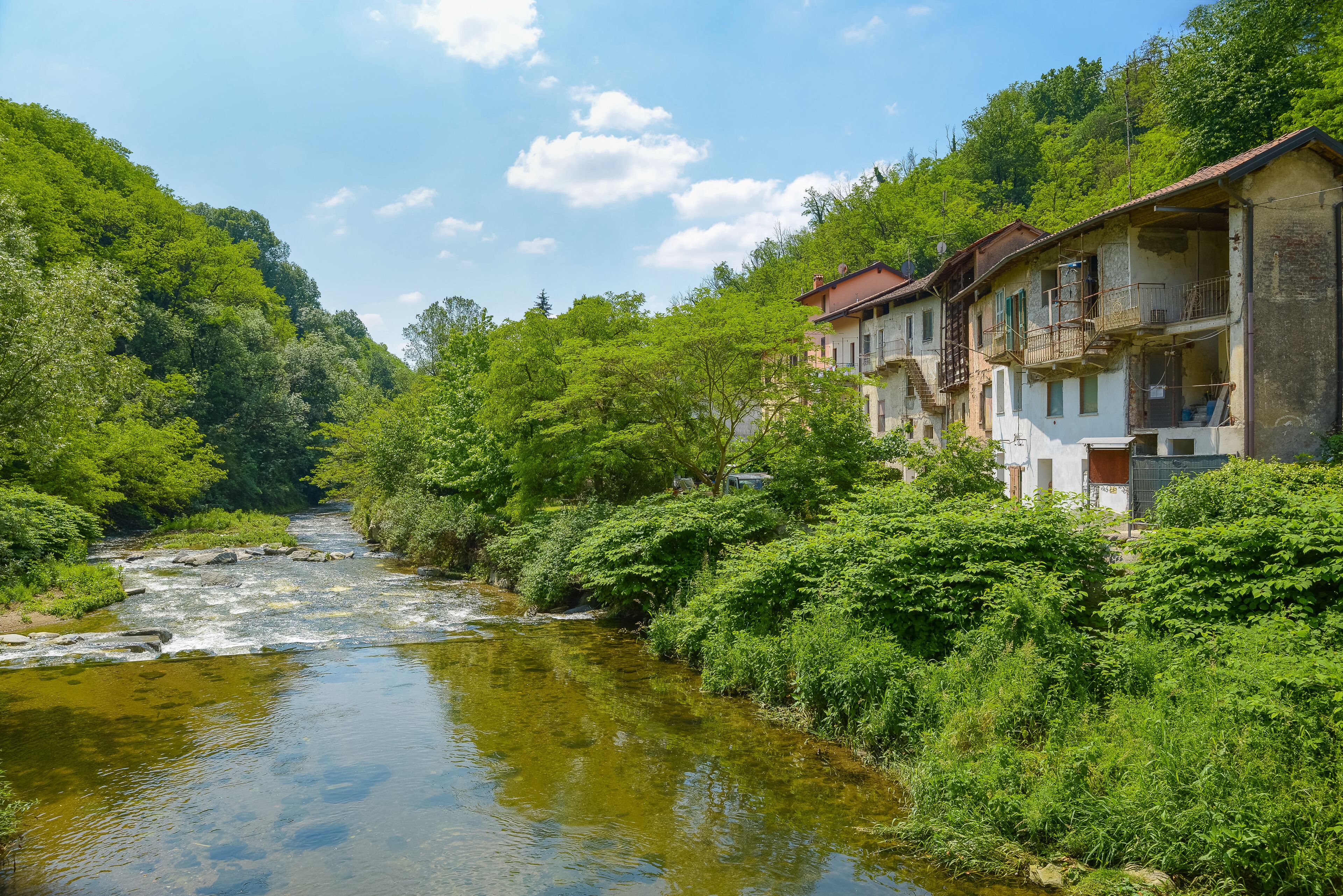 A river flowing through a lush valley with dense greenery and traditional buildings on the right.