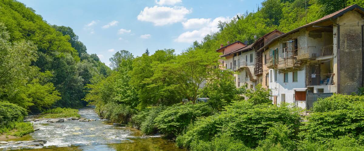 A river flowing through a lush valley with dense greenery and traditional buildings on the right.