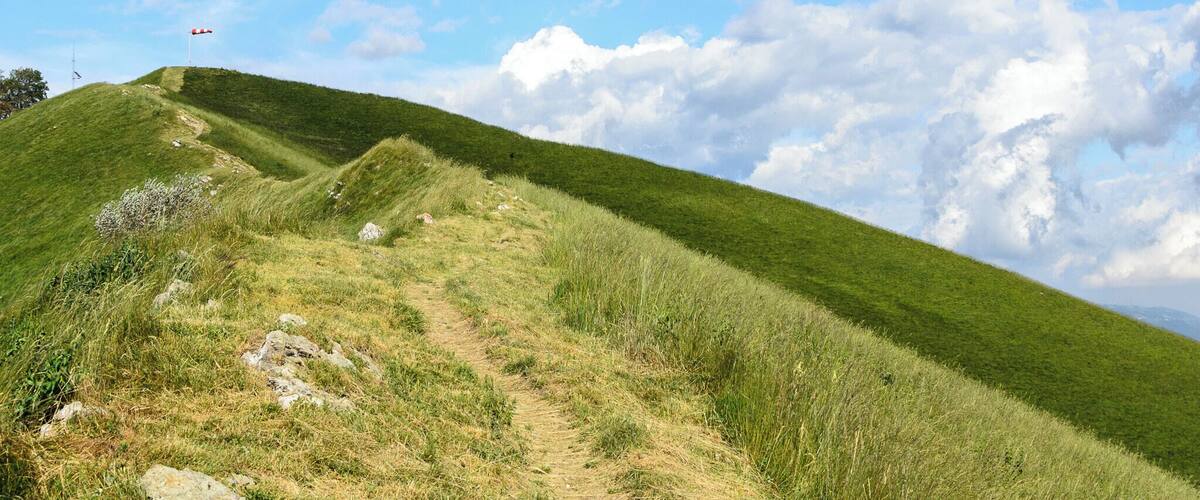 A grassy hill with a flag on top, a clear sky, and scattered clouds.