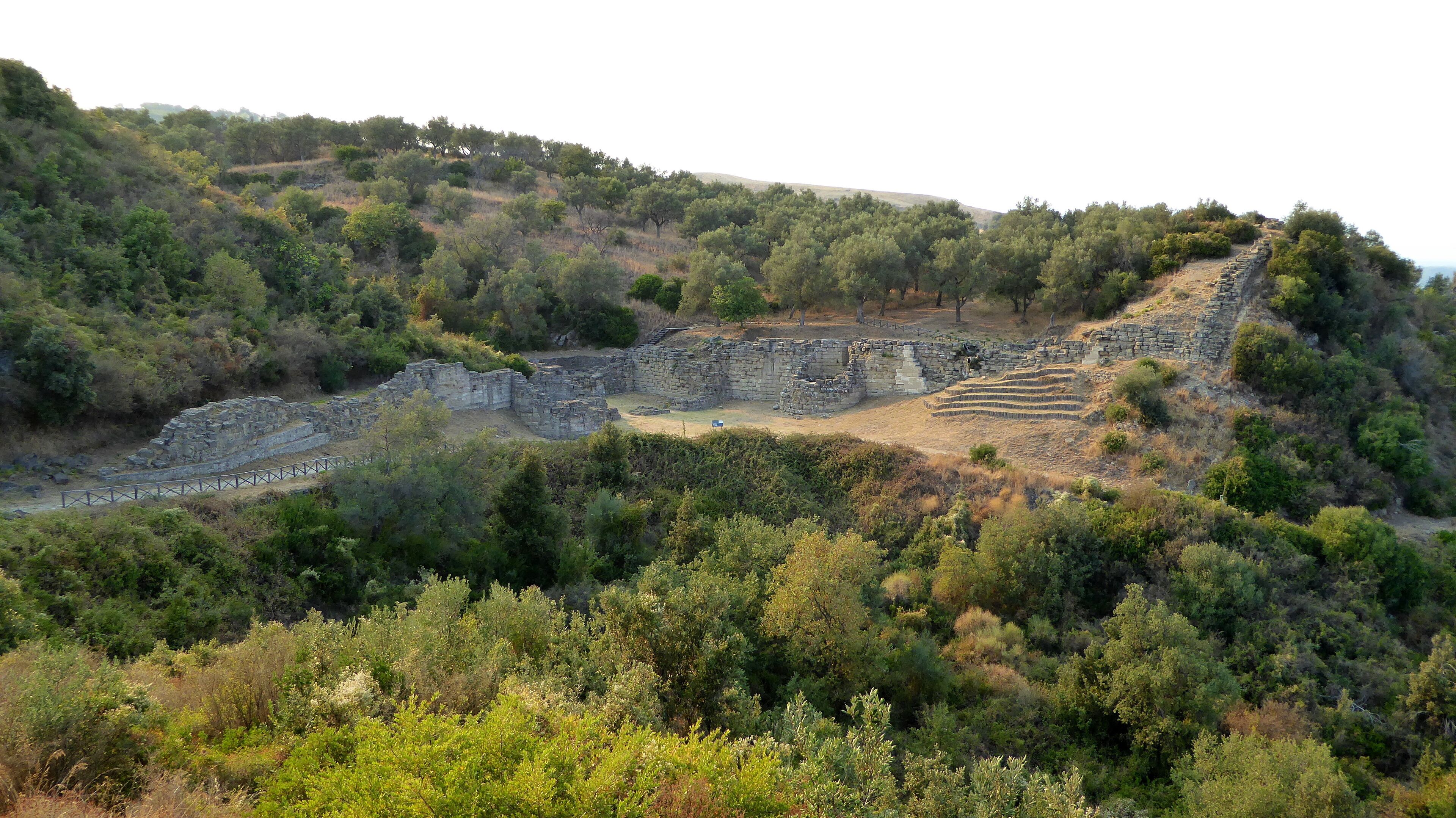 Ancient ruins on a hillside with dense vegetation.