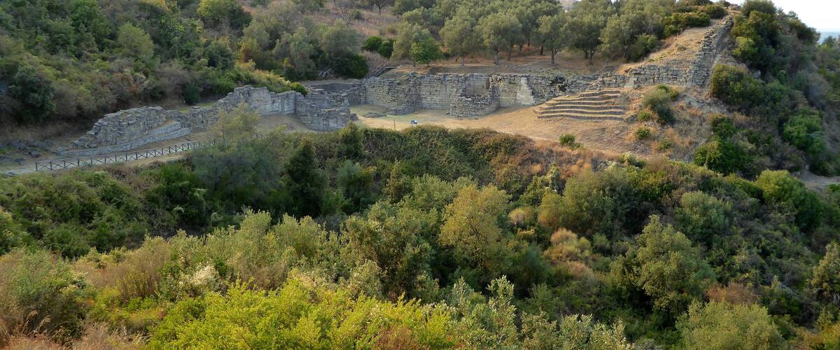 Ancient ruins on a hillside with dense vegetation.