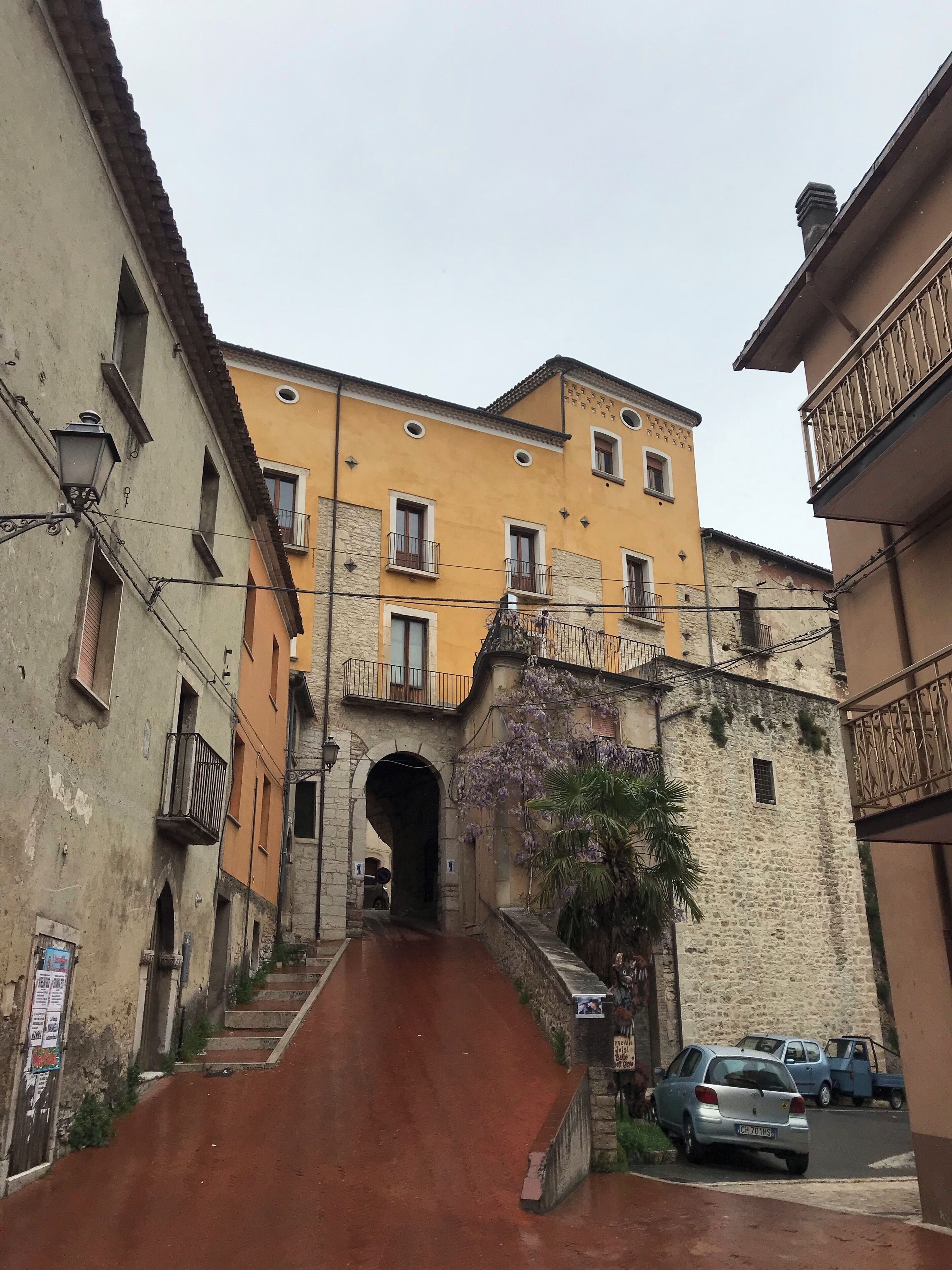 A narrow street with a steep incline leading to a yellow building with multiple windows and balconies.