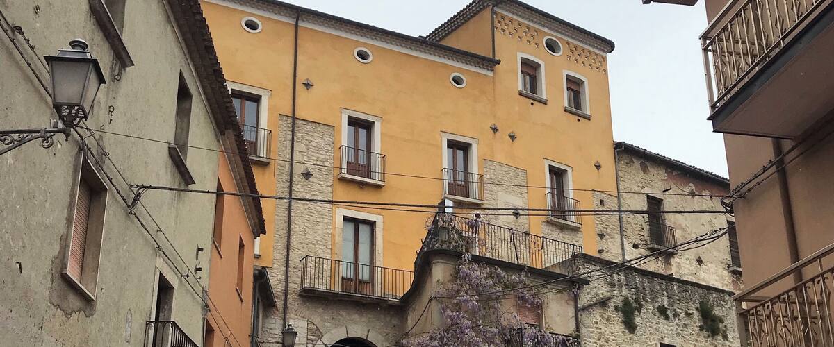 A narrow street with a steep incline leading to a yellow building with multiple windows and balconies.