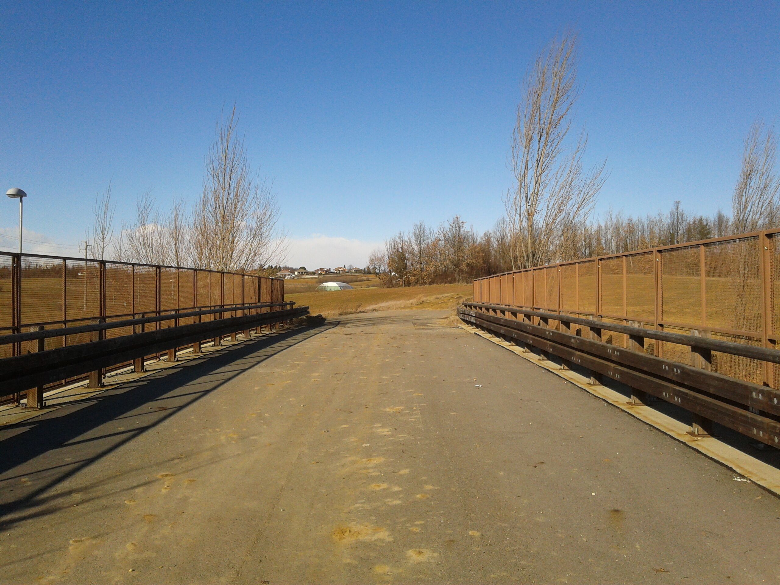 A rural road with a metal fence on both sides, leading to a white building in the distance.