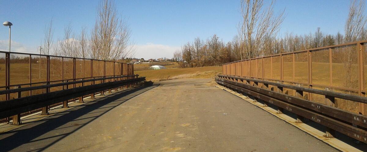 A rural road with a metal fence on both sides, leading to a white building in the distance.