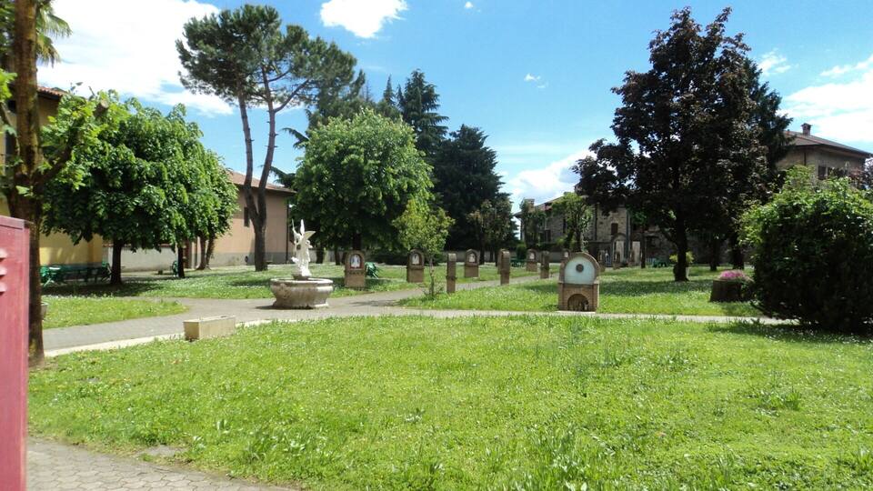 A cemetery with gravestones, a statue, and surrounding greenery.
