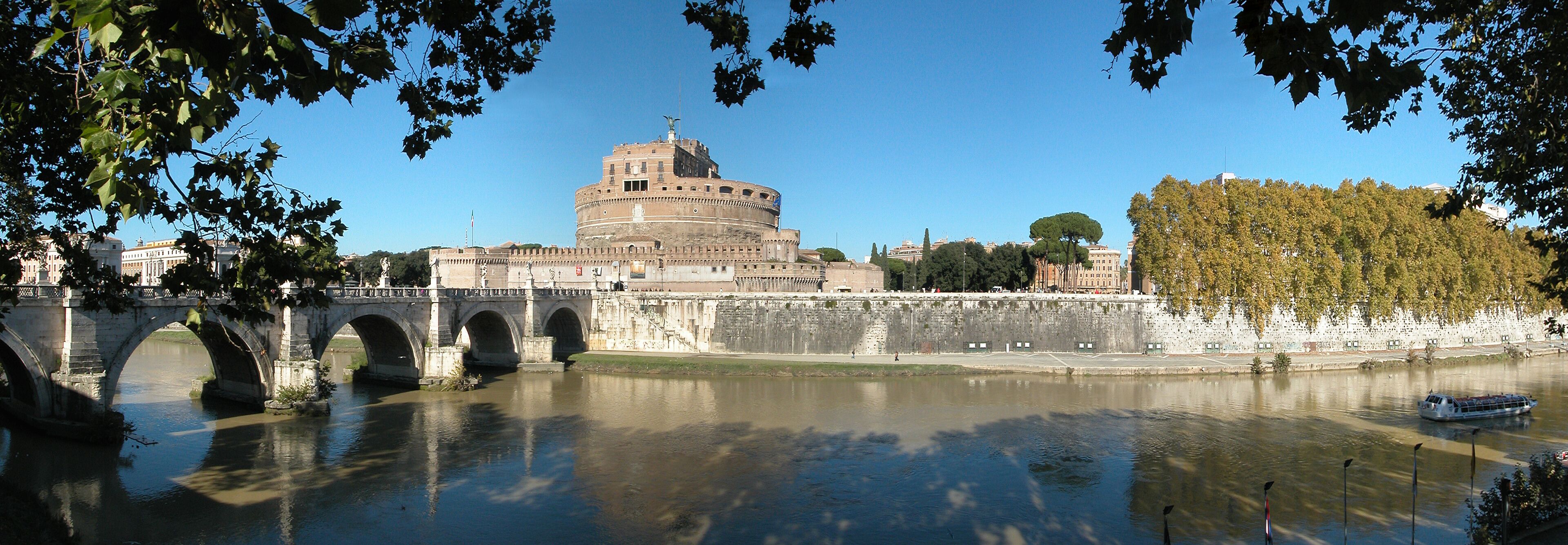 The Colosseum in Rome, Italy, with the Tiber River in the foreground and a bridge in the background.