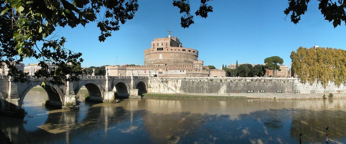 The Colosseum in Rome, Italy, with the Tiber River in the foreground and a bridge in the background.