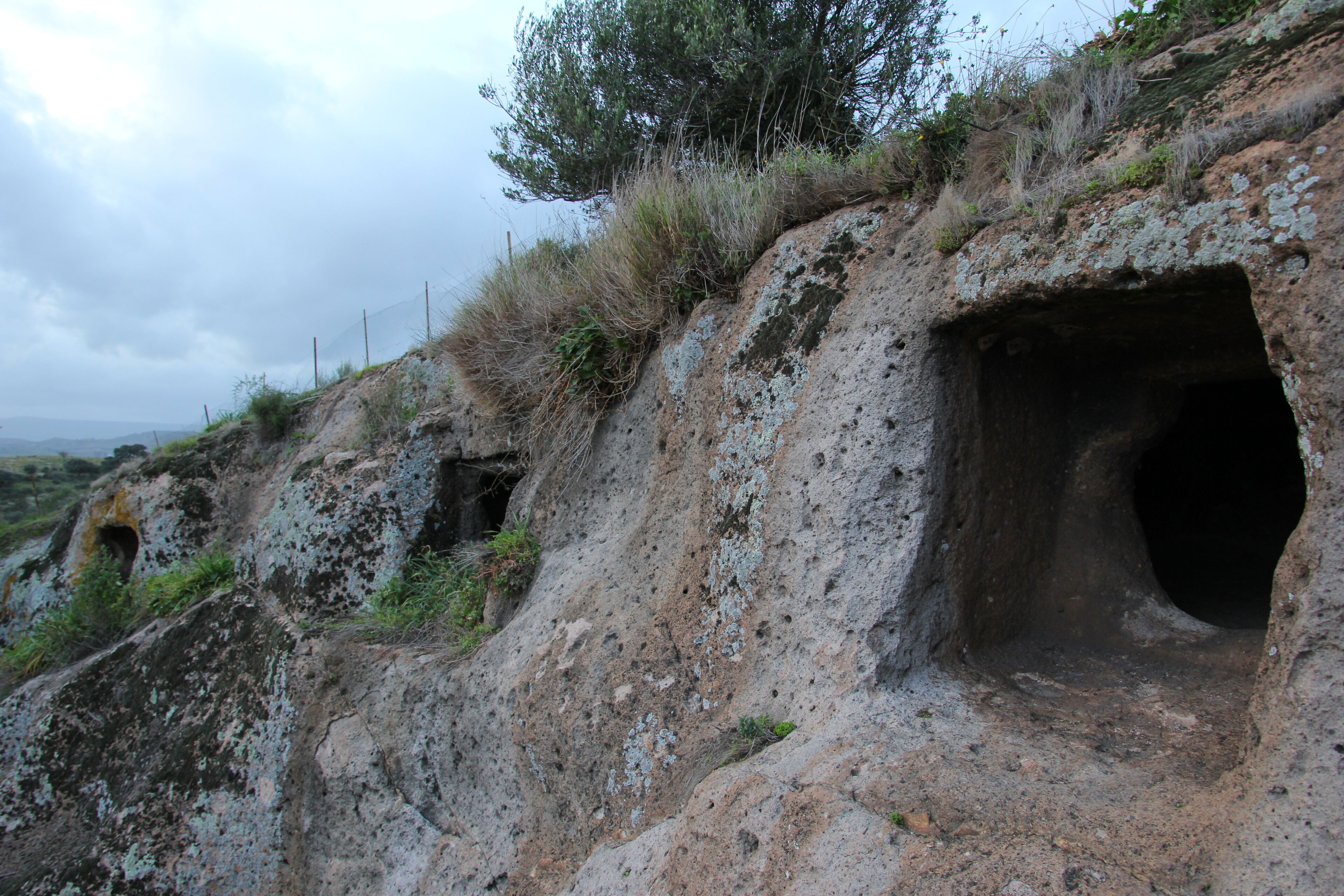 A rocky landscape with a cave entrance and sparse vegetation.
