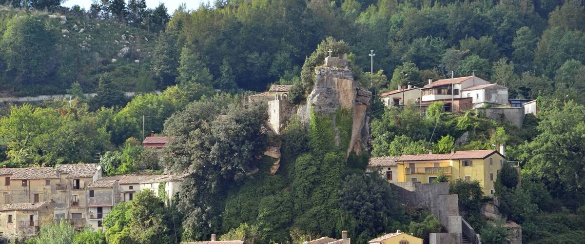 A hillside village with terraced houses, a prominent rock formation, and a church.
